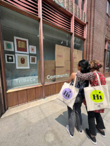 Two women with Hi tote bags outside Tribeca Community Center ENEF artwork gallery window