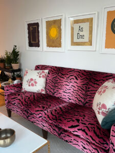 a row of artworks hanging on the wall including above a pink leapord print sofa, including As One artwork